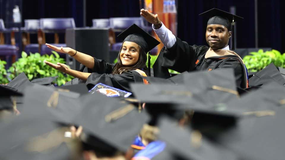 UF Warrington Graduates in cap and gown holding a #WarringtonGrad sign