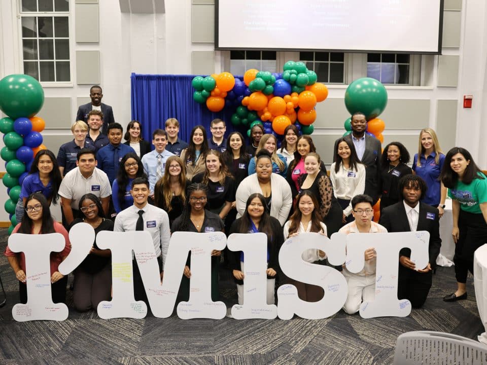 A large group of first generation students holding letters that read I'm 1st, with Jeff Danso in the background