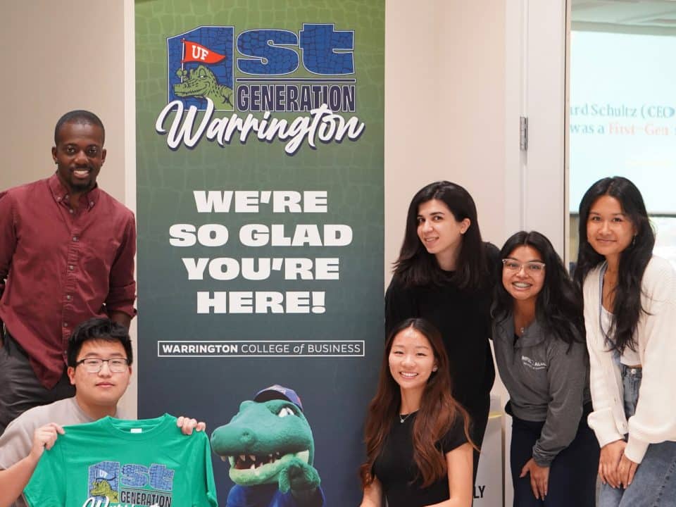 Jeff Danso and five first-generation students by a 1st Generation Warrington sign that says We're so glad you're here! One student holds up a 1st generation shirt.