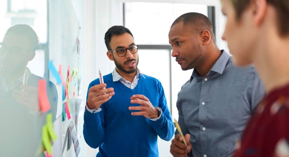 Three people talk by a whiteboad with sticky notes on it