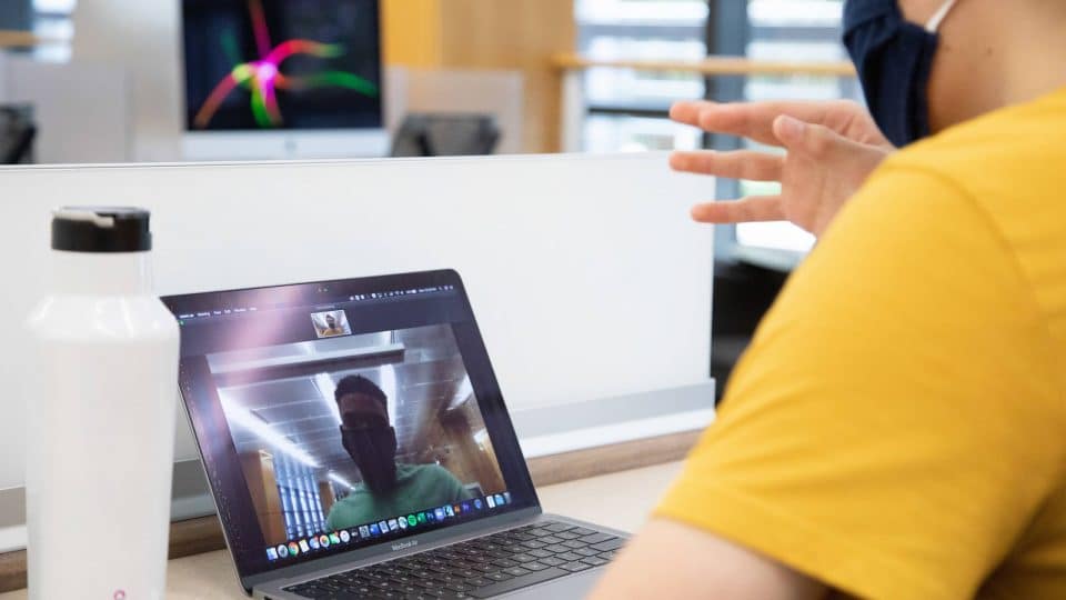 Two students with masks in a Zoom meeting shown on a laptop