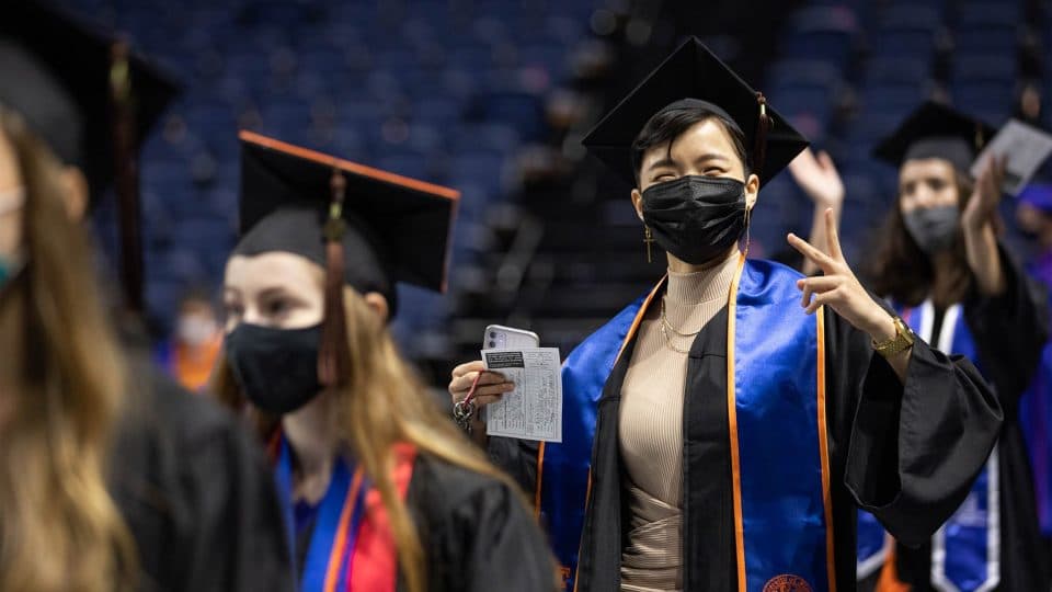 Graduate looks at the camera while others look on at the ceremony