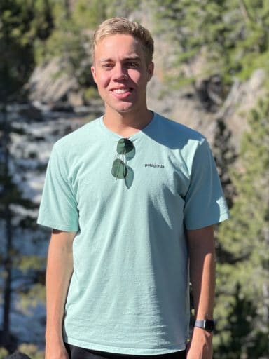 Ryan Bell with mountains, pines and a river behind him