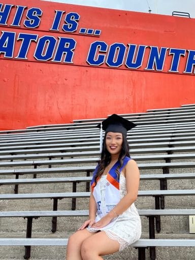 Sally Yang with her graduation cap in the stadium under the This is Gator Country sign