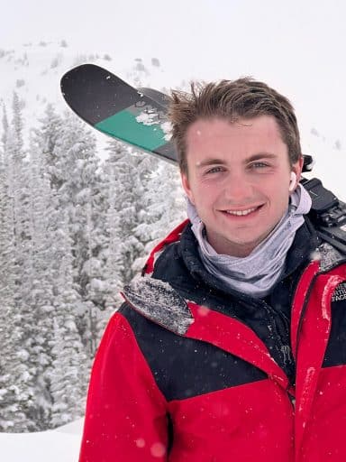 Caleb Pezzi with skis on his shoulder and a snowy mountain in the background