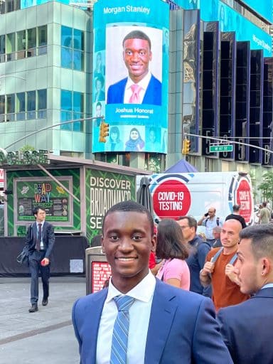 Joshua Honorat with a billboard displaying his name and photo in the background