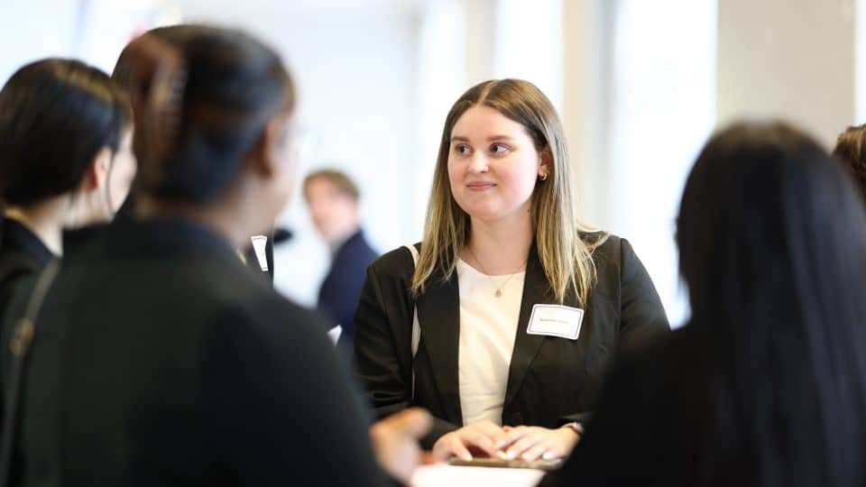 One student facing the camera is in focus while the others around a table converse with her