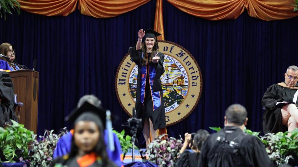 A student does the Gator Chomp on stage in her graduation attire