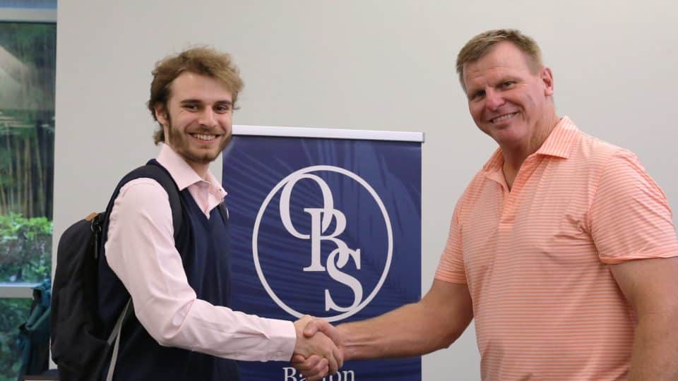 A student with a backpack shakes hands with an older gentleman