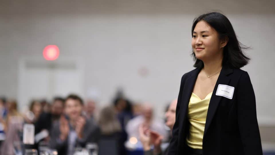 A student walks forward as others seated behind her applaud