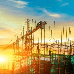 The sun rises behind a building construction site with busy workers and cranes