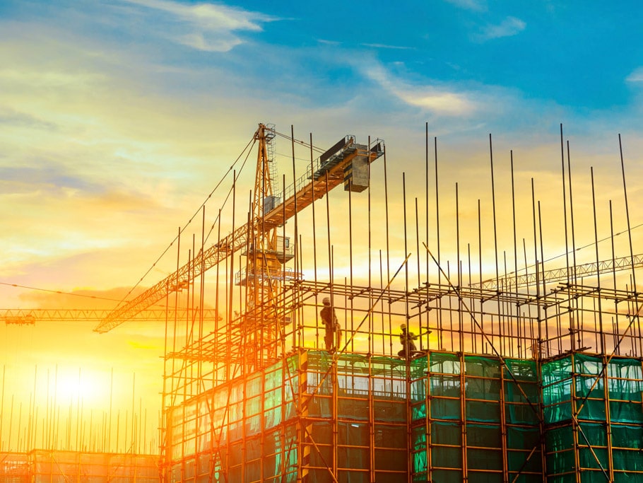 The sun rises behind a building construction site with busy workers and cranes