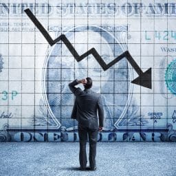 A man scratches his head while facing a giant dollar bill with a downward trending arrow on it