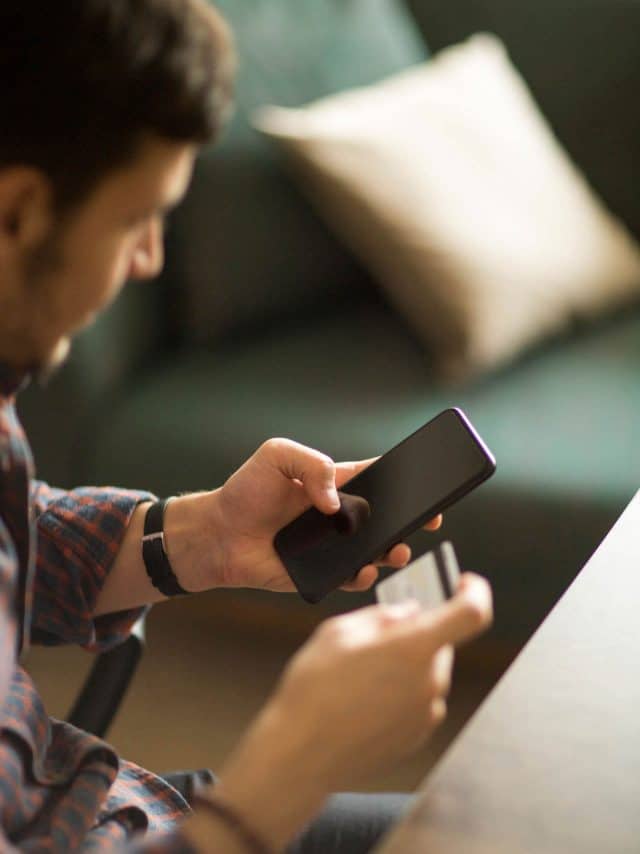 A man is holding a smartphone in one hand and a credit card in another as he completes a transaction