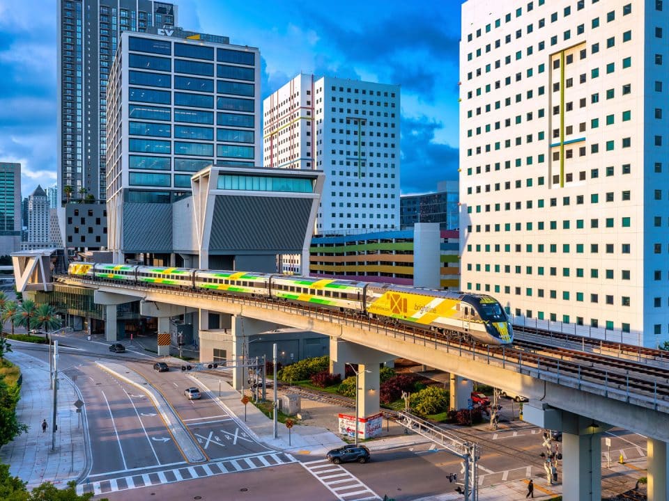 A passenger train departs MiamiCentral on an elevated track with tall buildings all around