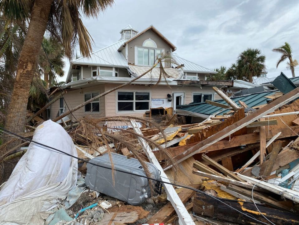 A large pile of building debris from Hurricane Ian in front of a damaged building