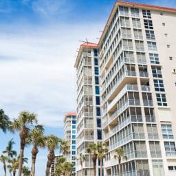 Tall condos with palm trees and wispy clouds on a blue sky