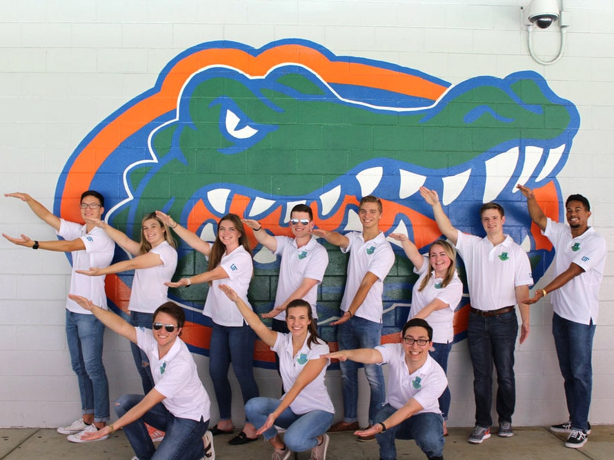 Group of HLC students Gator Chomp in front of a Gator logo on a wall