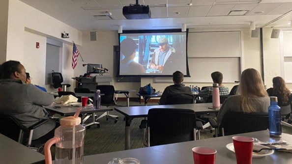 Students watch a movie projected onto a screen at the front of a classroom