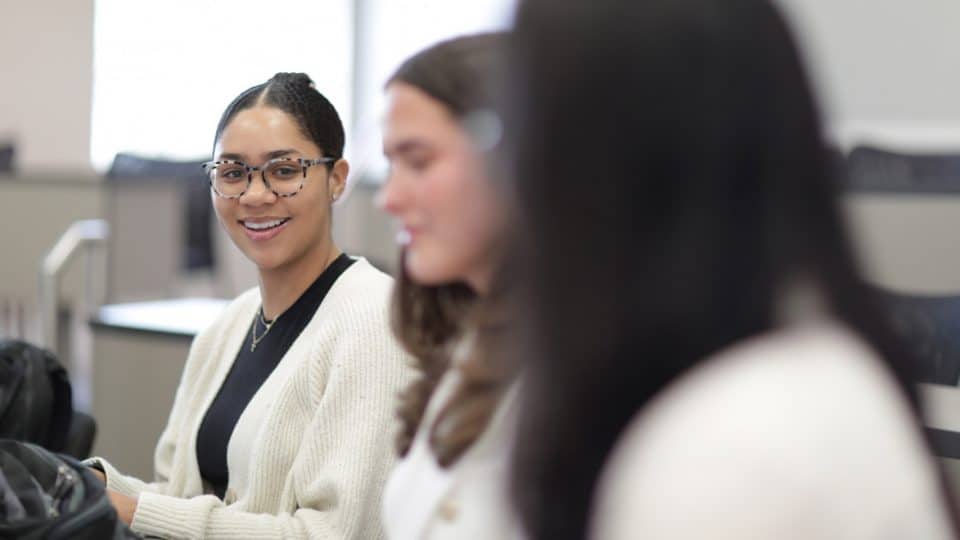 A student in focus is smiling toward the camera with two other students in the foreground