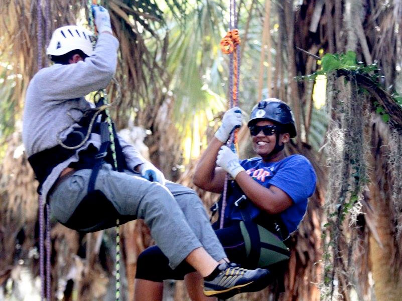 Two MSE students hang from climbing ropes in the trees