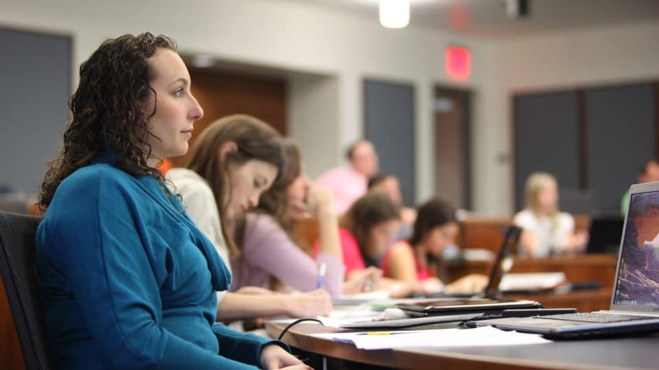 In a classroom a woman listens with several other students in the background