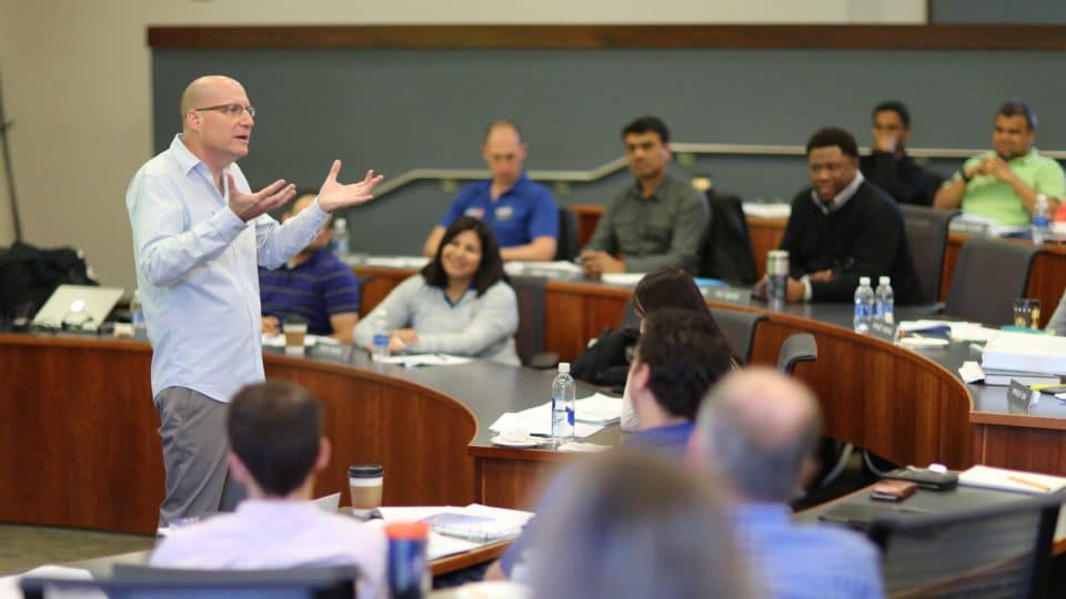 The instructor speaks to the classroom while students listen