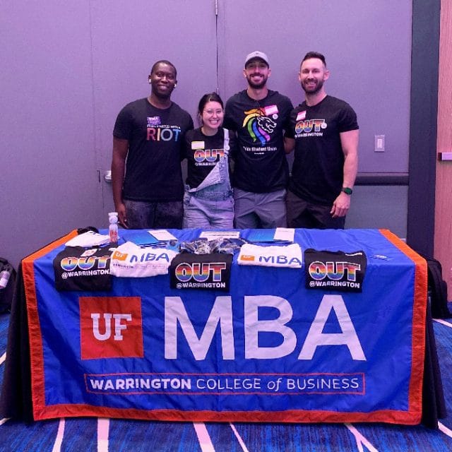 Four Out@Warington students behind a display table at the Pride Student Union Welcome Assembly