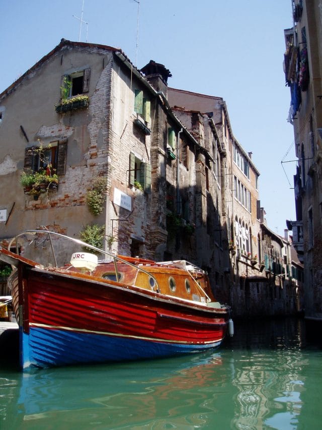 Red and blue boat docked along the watery streets of Venice, Italy