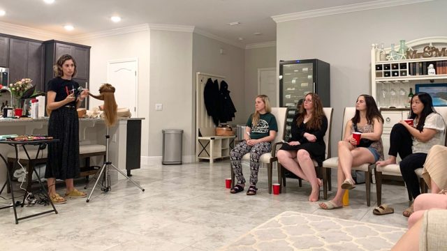 Women watch as a former hairstylist gives a presentation on curling, braiding, and styling