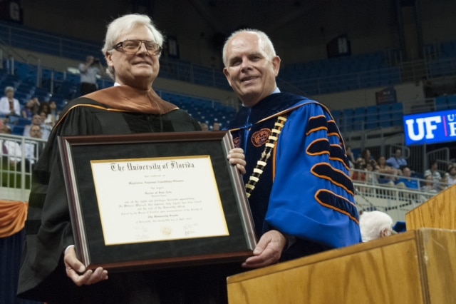 John Dasburg holds a framed honorary Doctor of Commerce with Bernie Machen at the graduation ceremony in spring 2014 at the O'Connell Center