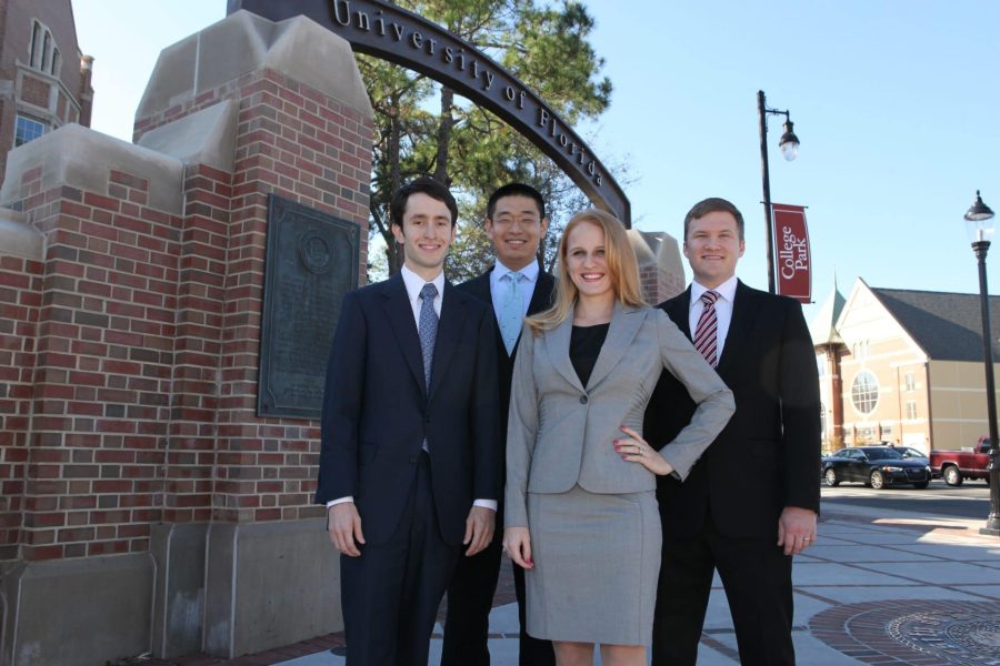 Four members of a Case Competition Team stand by the University of Florida gateway at 13th Street and University Avenue