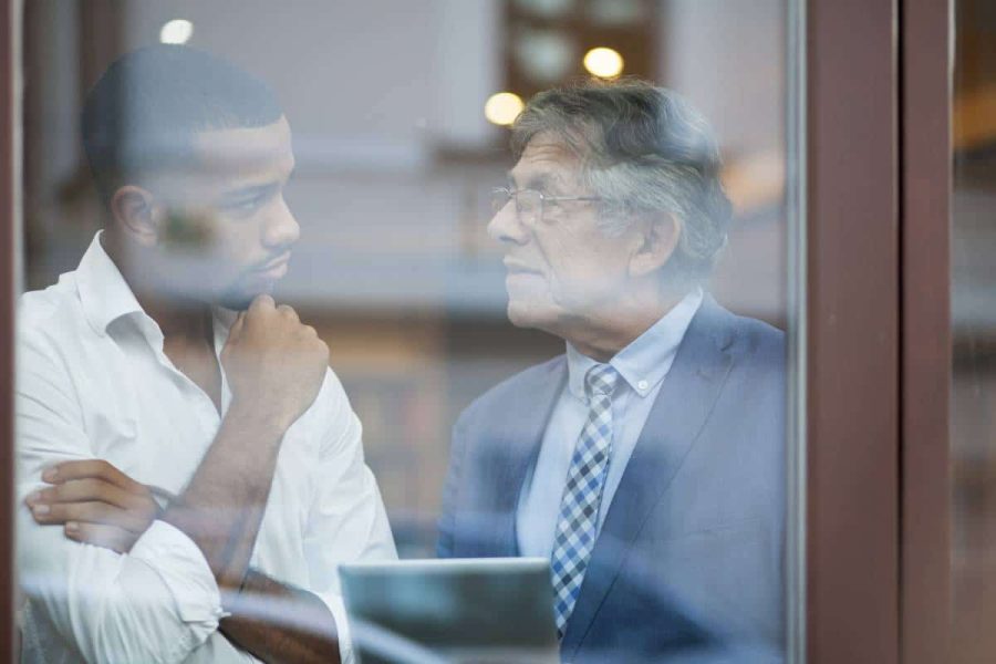 View through a window of two men, one young and one older, having a discussion