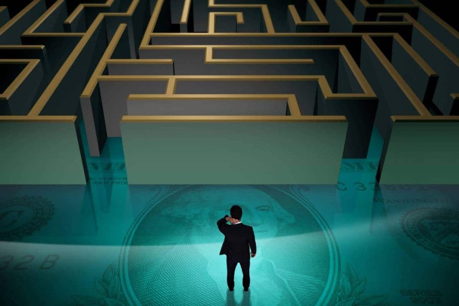 Birdseye view of a man standing on a large dollar bill looking confused as he enters a maze