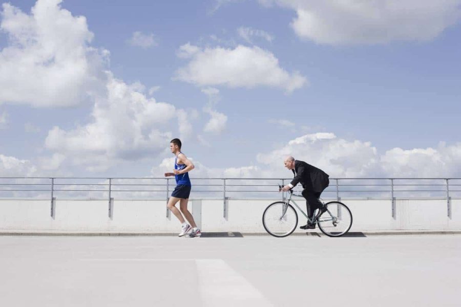 Man running in athletic clothing followed by a man wearing a business suit on a bicycle