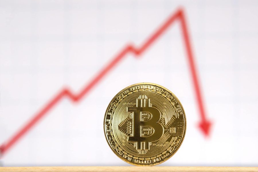 A golden bitcoin in front of a red graph line that rises and then sharply drops, indicating a drop in value