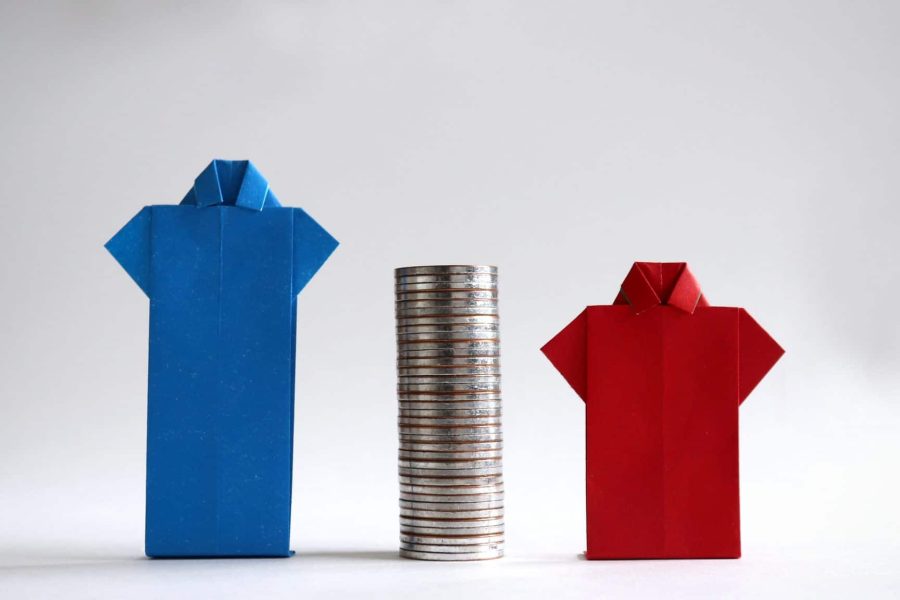 Blue and smaller red paper folded in the shape of shirts with a pile of coins in between to represent the concept of gender employment and wage gap