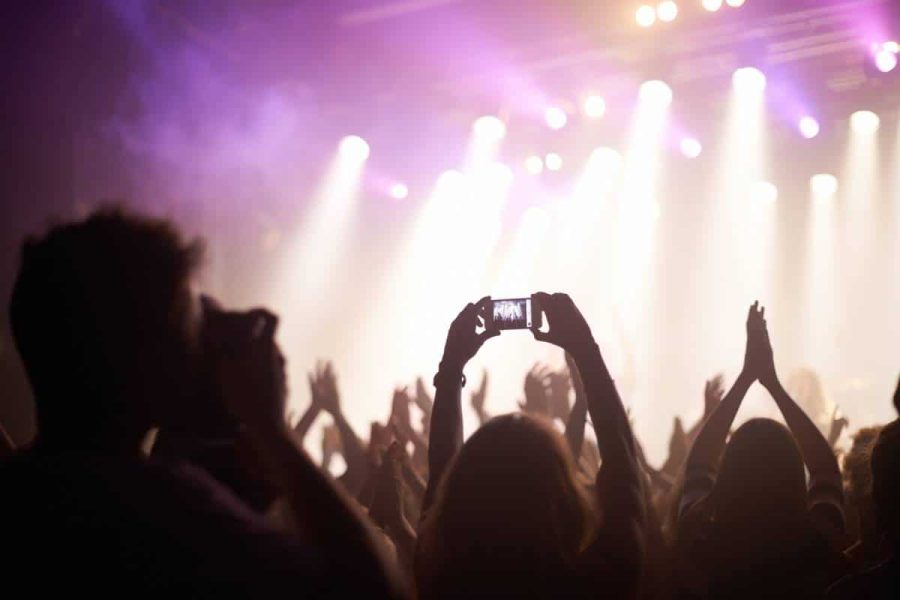 Person standing in a crowd at a concert holding their phone up high to take a photo or video of the stage
