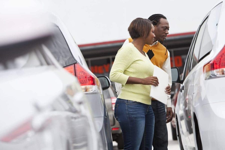 Man and woman looking at cars at a dealership and trying to make a decision about which to buy or lease.