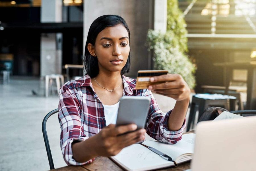 A young woman using a cellphone and credit card outside at a table