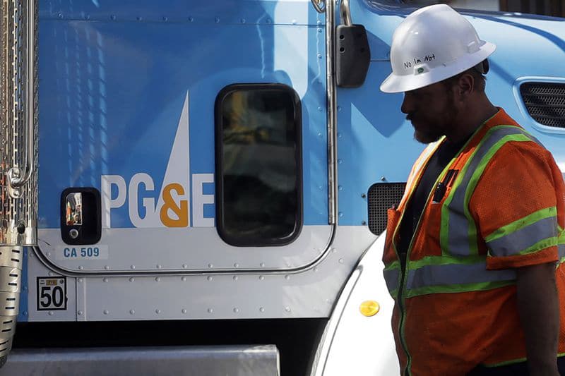 A worker with a hardhat stands next to a PG&E truck
