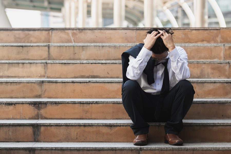 Young business man in suit with hands on bowed head and suit jacket over his shoulders sitting on stairs