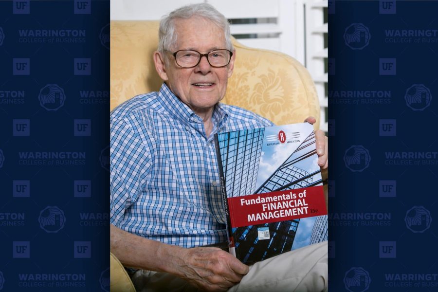 Eugene Brigham sits in a chair holding a copy of his textbook Fundamentals of Financial Management