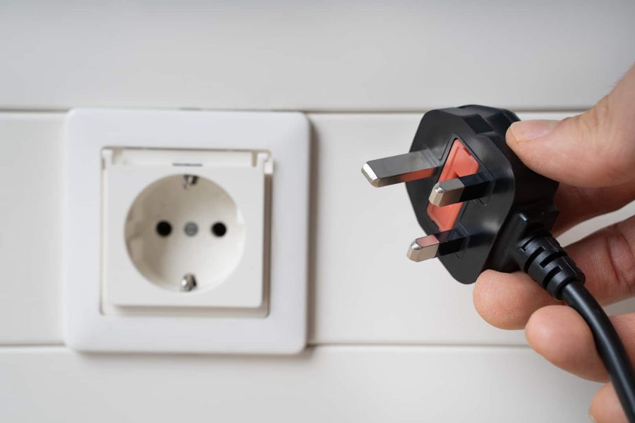 Hand holding incompatible AC plug near wall socket