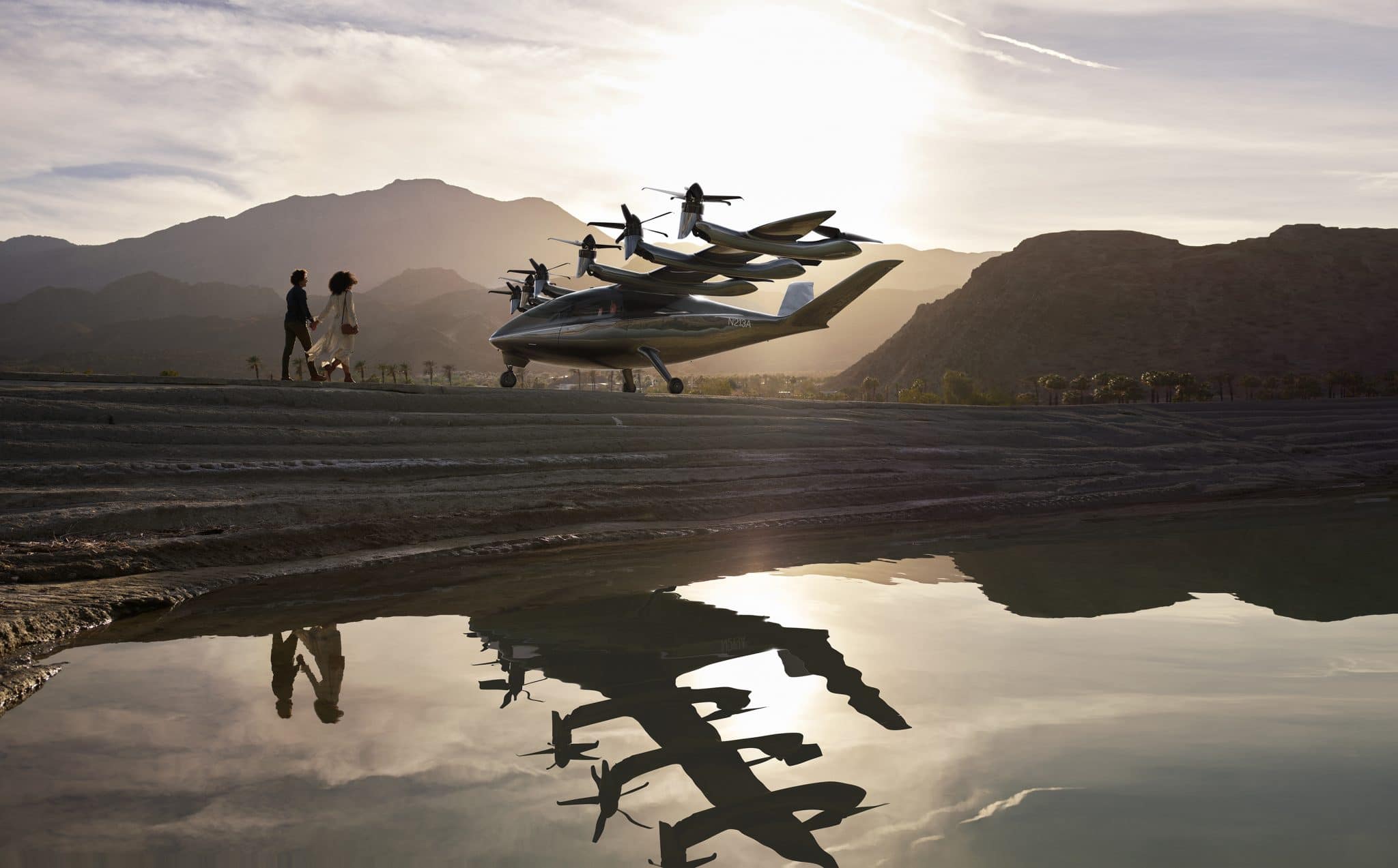 Small eVTOL landing in front of mountains. Two people stand in front.