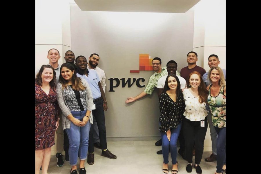 PwC's incoming internships pose by their logo on the wall