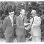 Two men pose for a photo with Robert Lanzillotti as one shakes Lanzillotti's hand while handing him a check