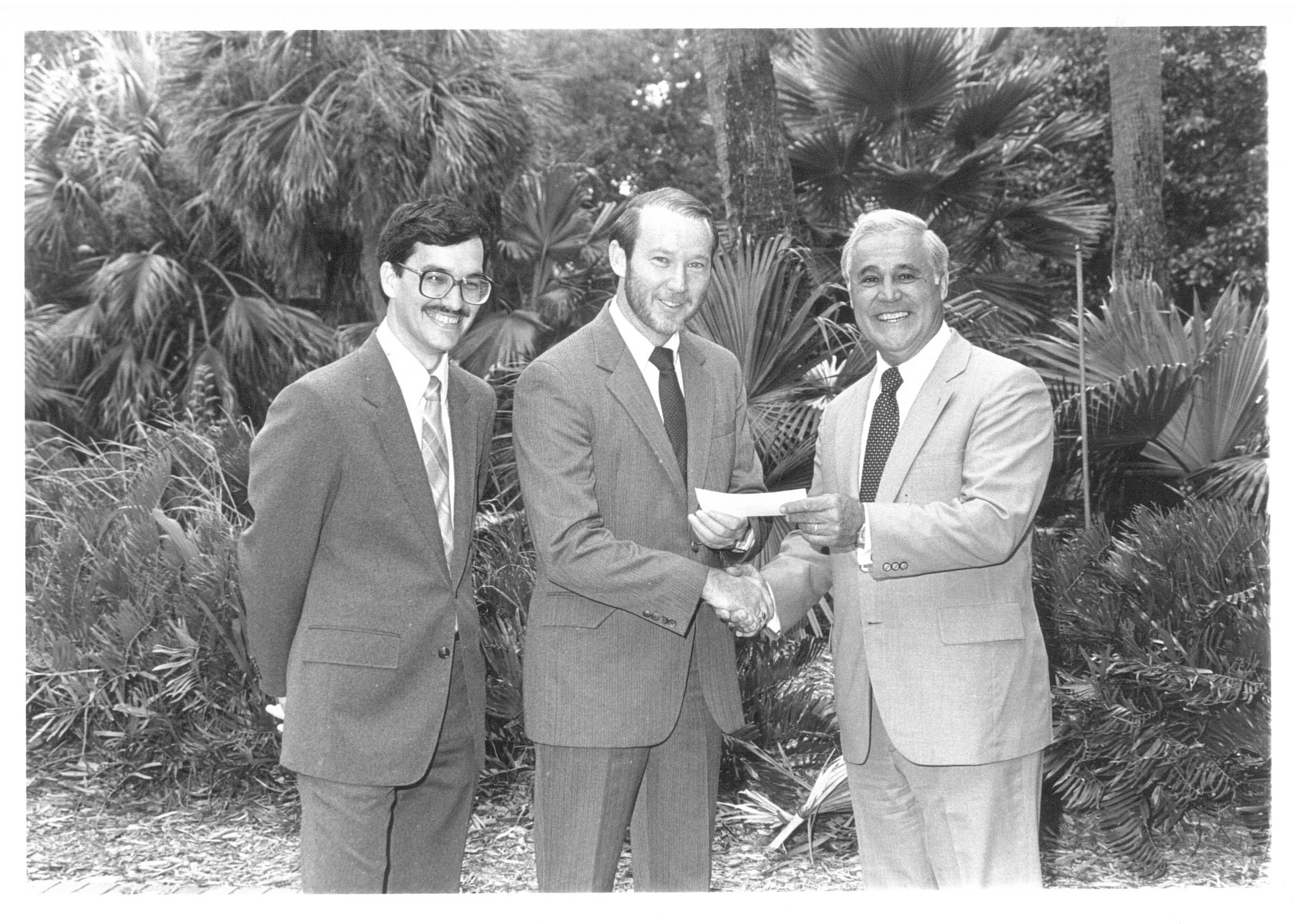 Two men pose for a photo with Robert Lanzillotti. One shakes Lanzillotti's hand while handing him a check.