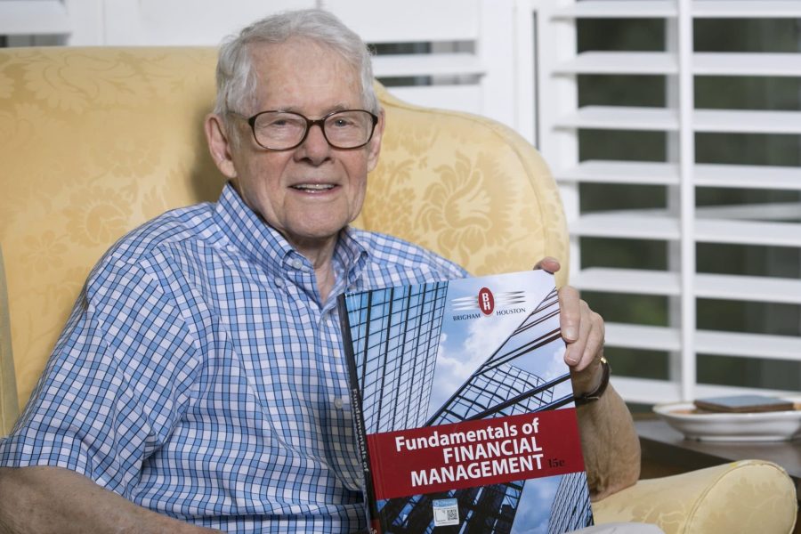 Gene Brigham seated in an armchair holds his book Fundamentals of Financial Management