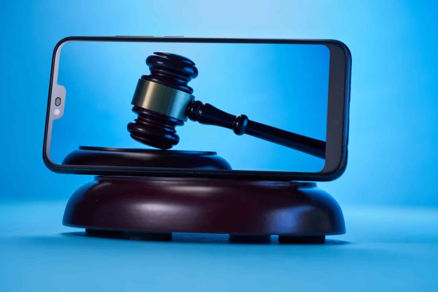 Gavel hammer with a blue background pictured on a smartphone laying on its side on top of a sound block also with a with blue background